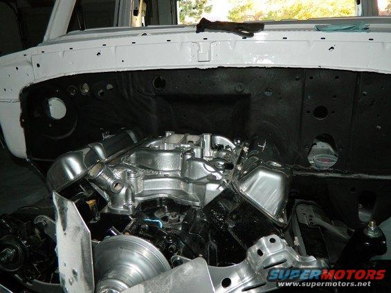 Engine bay with a polished V8 engine, fan, and pulleys. White firewall and black inner fenders visible