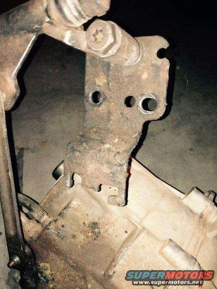 Close-up of a rusty metal bracket attached to a beige transfer case housing