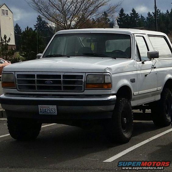 White Ford Bronco with a dented front fender and aftermarket wheels, viewed from the front three-quarter angle