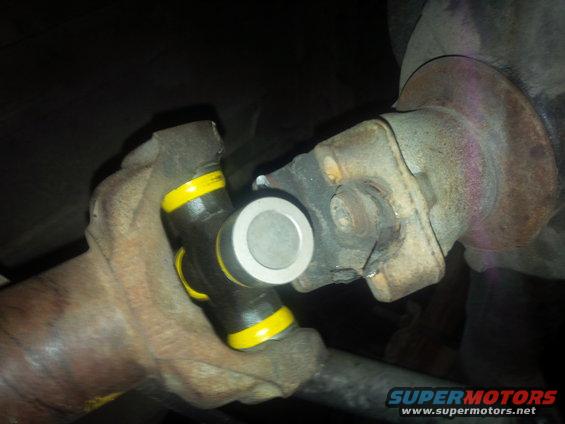 Universal joint with yellow bands and a silver cap, attached to a rusty flange