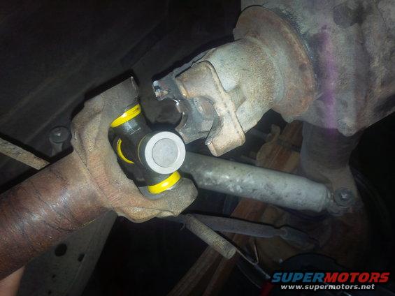 Driveshaft universal joint with yellow and black components, attached to a rusty metal component