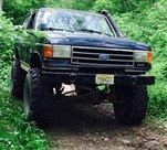 Dark blue Ford F-Series truck with lifted suspension and large tires, seen from the front