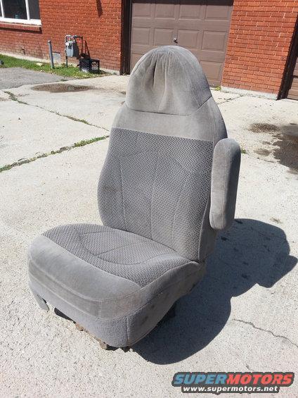Gray fabric car seat with armrest, sitting on concrete