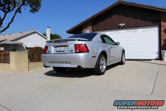 Silver 2002 Ford Mustang parked in front of a garage, rear view. License plate reads 4VOM193