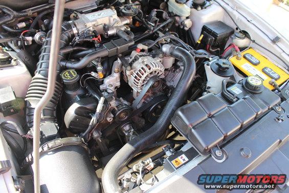 Engine bay of a 2002 Ford Mustang, showing the V8 engine, yellow battery, and various hoses and components