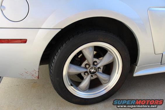 Silver Ford Mustang rear wheel and fender with a red reflector on the side