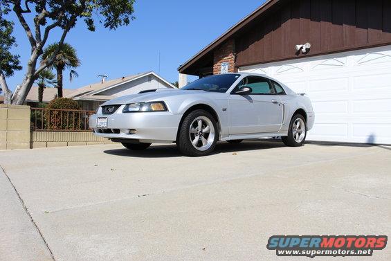 Silver coupe parked in a driveway, front quarter view. Hood scoop and aftermarket wheels visible