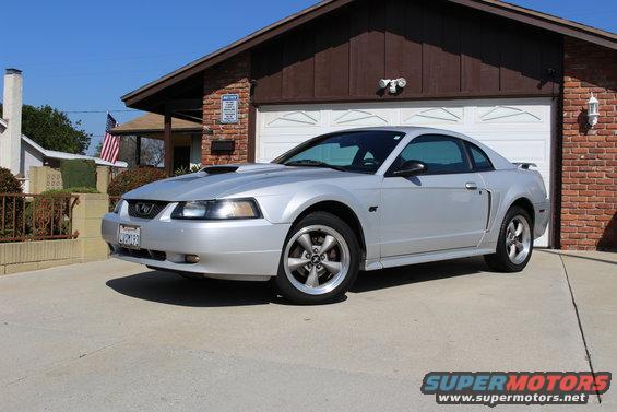 Silver 2002 Ford Mustang parked in driveway in front of a brick house