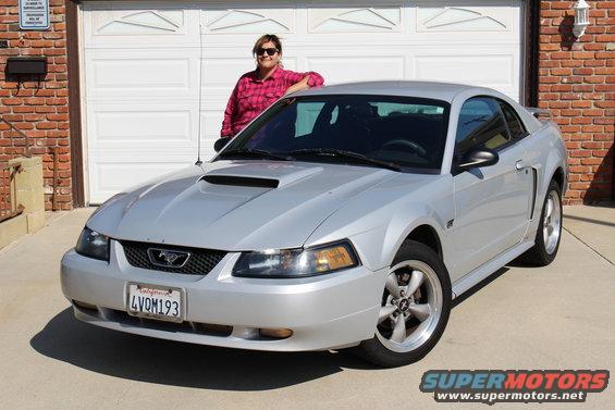 Silver 2002 Ford Mustang parked in front of a garage with a woman leaning on the hood