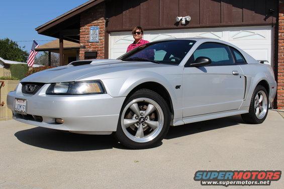 Silver 2002 Ford Mustang GT parked in front of a garage with a woman standing by it