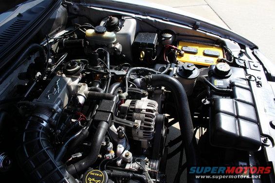 Engine bay of a 2002 Ford Mustang, showing the V8 engine, battery, and hoses