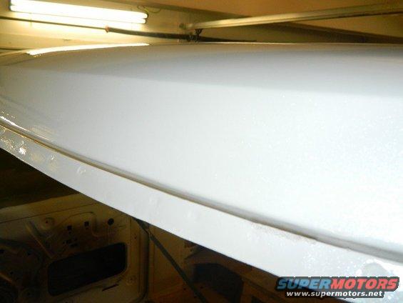 Close-up of white paint on the inside of a vehicle's roofline, showing some texture. Interior structure is visible below