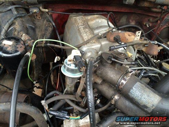 Engine bay with hoses, wires, and a metal intake manifold. Some parts are dirty and worn