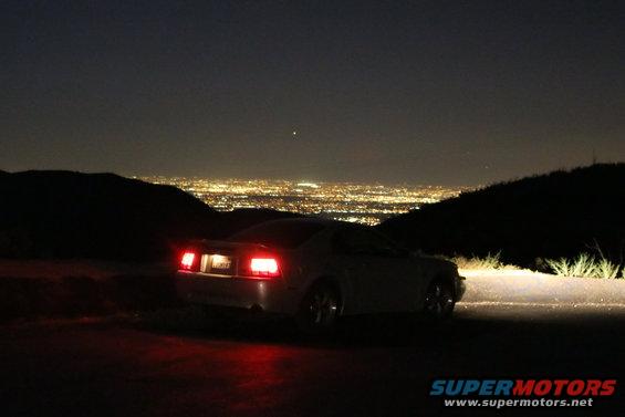 Rear of a 2002 Ford Mustang parked at night with city lights in the background