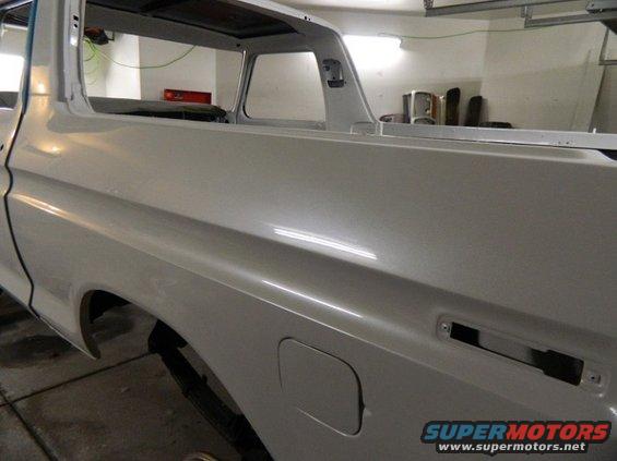 1979 Ford Bronco body, side view, in garage. White paint, rear fender, fuel door, and window frame visible