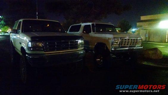 Two white Ford SUVs parked at night. The one on the right is a 1979 Ford Bronco