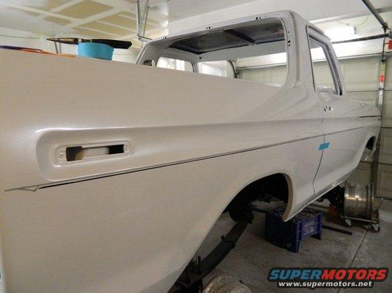 White 1979 Ford Bronco body on jack stands, undergoing restoration. The rear quarter panel and bed are visible