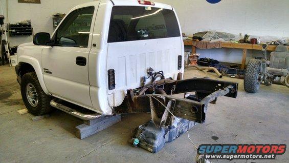 White pickup truck chassis on blocks, fuel tank below, workshop background