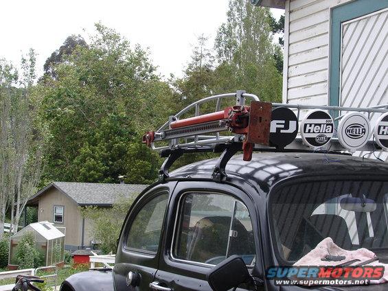Black 1964 Volkswagen Beetle with a roof rack carrying a Hi-Lift jack and Hella lights