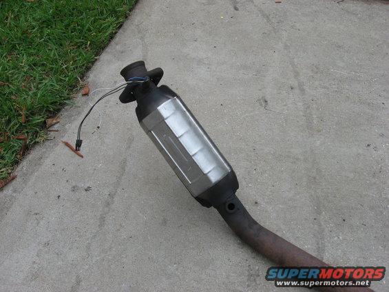 Exhaust catalytic converter with wires attached, lying on concrete next to grass