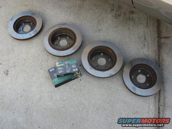 Four brake rotors and two boxes of brake pads on a concrete surface