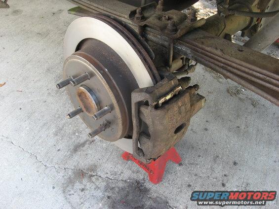 Rear brake caliper and rotor assembly on a red jack stand, showing leaf springs above