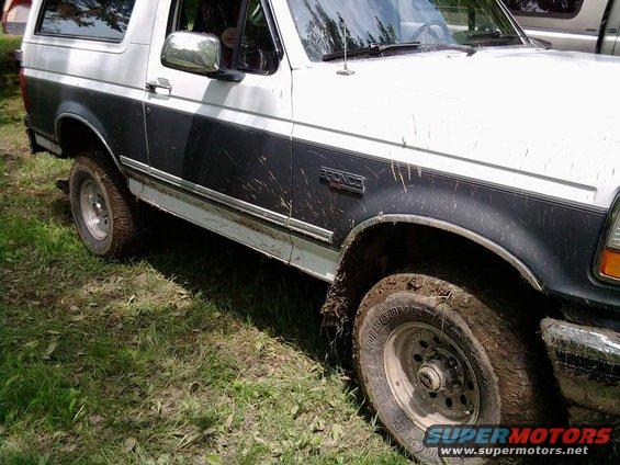 1993 Ford Bronco covered in mud, parked on grass