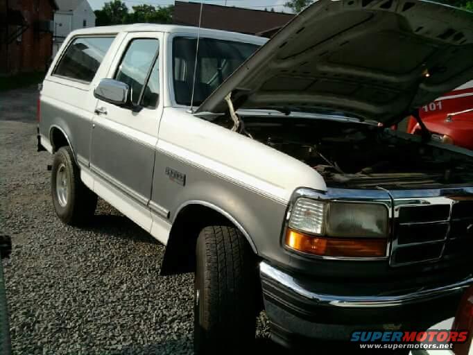 Two-tone white and grey SUV with hood open, parked on gravel