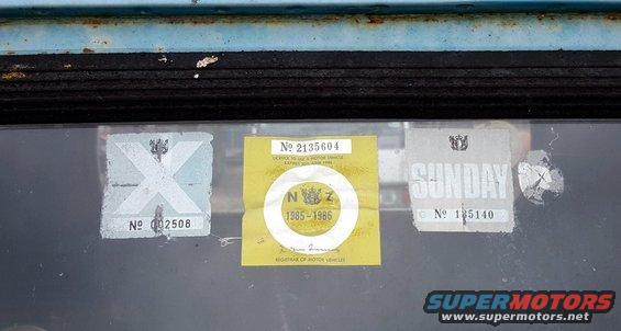 Three stickers on a window: one with an X, a yellow one showing 1985-1986, and a white one with SUNDAY