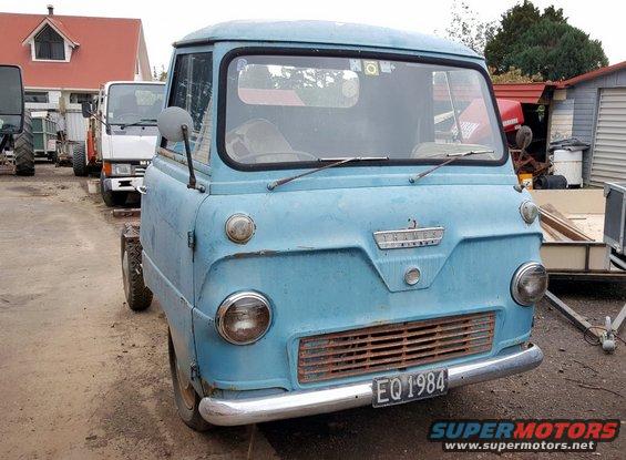 Light blue van with a chrome bumper and a rusted grille, parked outdoors