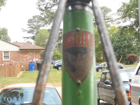 Green bicycle frame with a red and black emblem reading "Roll" is in focus, obscuring a residential scene with cars