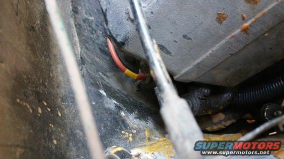 Close-up of red and yellow wires in a dirty engine bay with black corrugated tubing