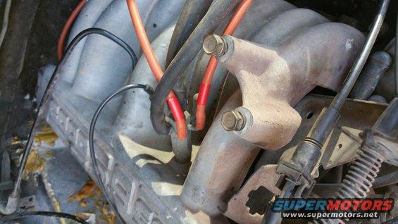 Engine manifold with orange spark plug wires and black cables. Some red tape on wires