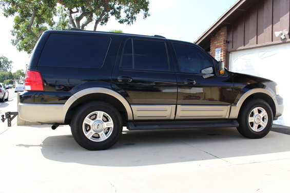 Side view of a black Ford Expedition with tan lower trim and tinted windows parked in a driveway