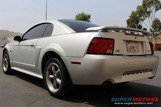 Silver Ford Mustang GT parked on asphalt, rear view showing taillights, spoiler, and 'Mustang' text on bumper