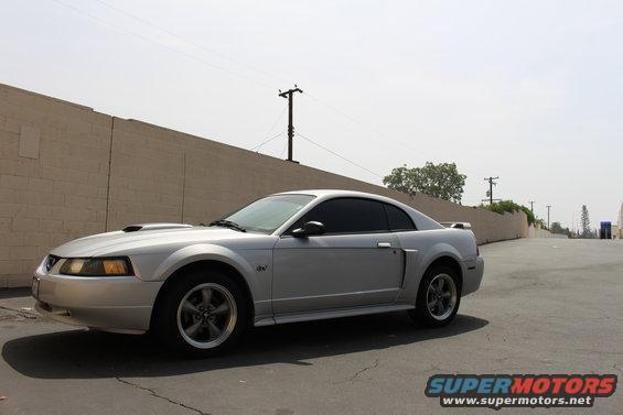 Silver 2002 Ford Mustang coupe parked on asphalt, 3q-front view. Hood scoop, tinted windows, and alloy wheels are visible