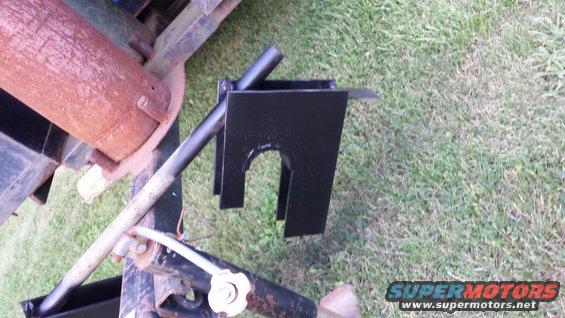 Black metal trailer hitch component with a rusty pipe attached, on grass