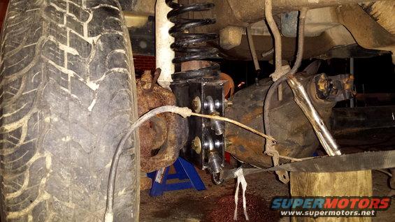 Close-up of vehicle's rear suspension with tire, coil spring, and differential visible