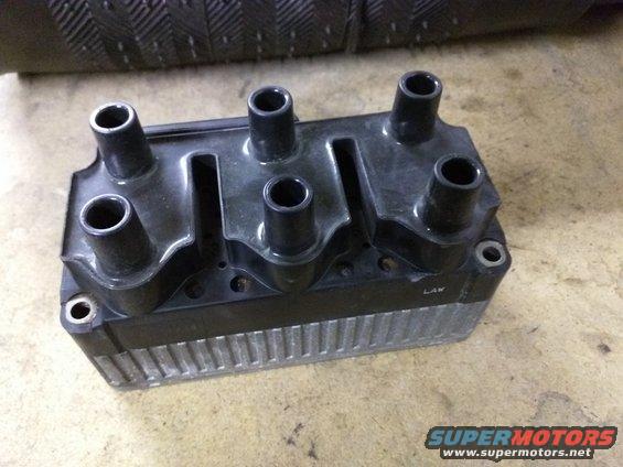 Ignition coil pack with four spark plug wire boots. Some text is visible on the side