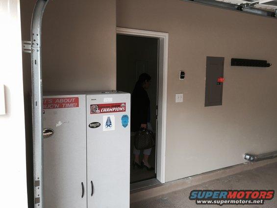 Garage interior with two tall storage cabinets, one with 'CHAMPIONS' sticker. Person walks through doorway