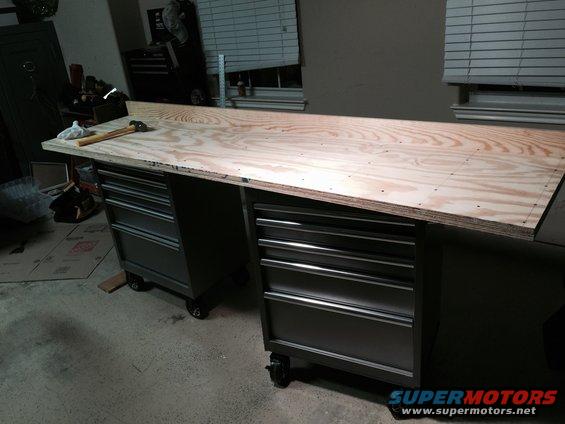 Workbench with plywood top over two rolling tool chests. Hammer and cloth on top