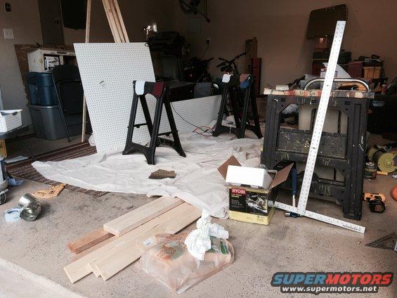 Garage scene with lumber, pegboard, sawhorses, and tools on a concrete floor