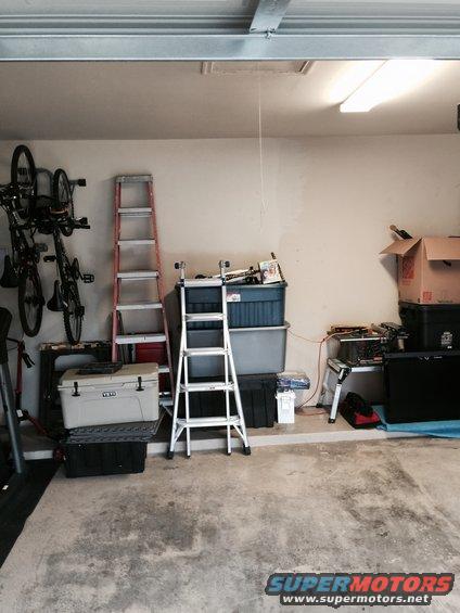 Garage interior with bicycles on wall mount, ladders, storage bins, and a cooler