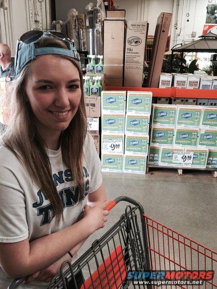 Woman in a store aisle with a shopping cart, surrounded by shelves of Clorox bleach and other products
