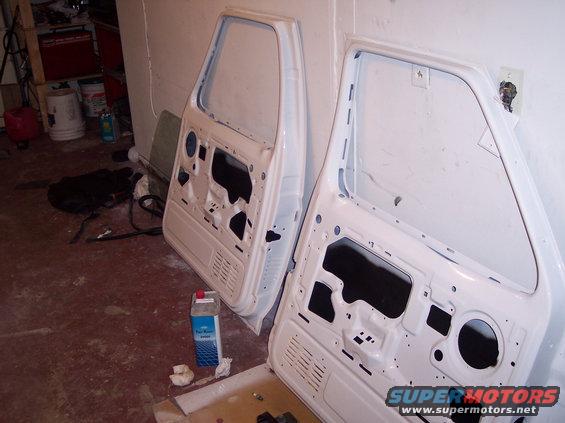 Two white vehicle doors disassembled, leaning against a wall in a garage