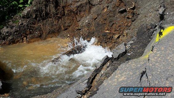 Eroded road with water flowing through a crack, marked with yellow paint