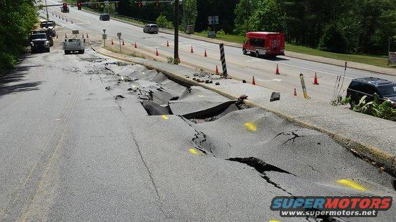 Road collapsed with debris, traffic cones, and vehicles on the side