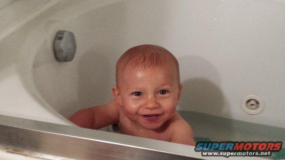 Baby smiling in a bathtub with a "Supermotors.net" logo visible