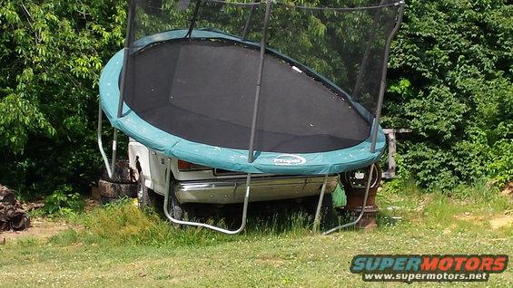 White truck with a trampoline resting on its front end, parked outdoors