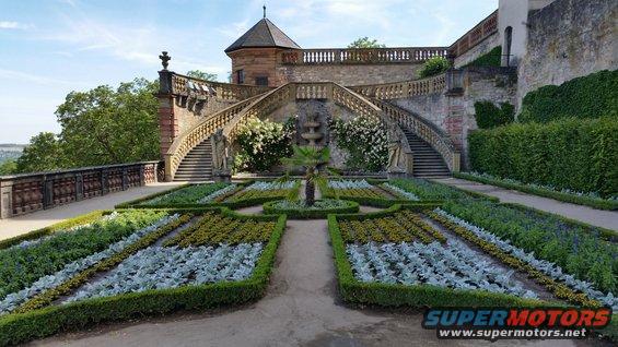 Ornate garden with formal flower beds and a grand staircase leading to a castle